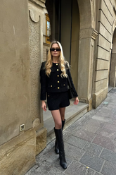 a lady wears a black tweed jacket with matching shorts and high boots
